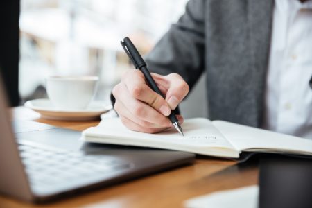 cropped-image-businessman-sitting-by-table-cafe-with-laptop-computer-writing-something (1)