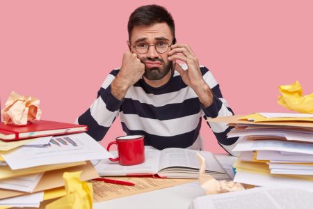 homem-estressante-e-descontente-tem-a-barba-por-fazer-conversa-ao-telefone-sente-se-cansado-de-trabalhar-muito-tempo-vestido-com-um-macacao-listrado-senta-se-na-mesa-com-papeis (1)